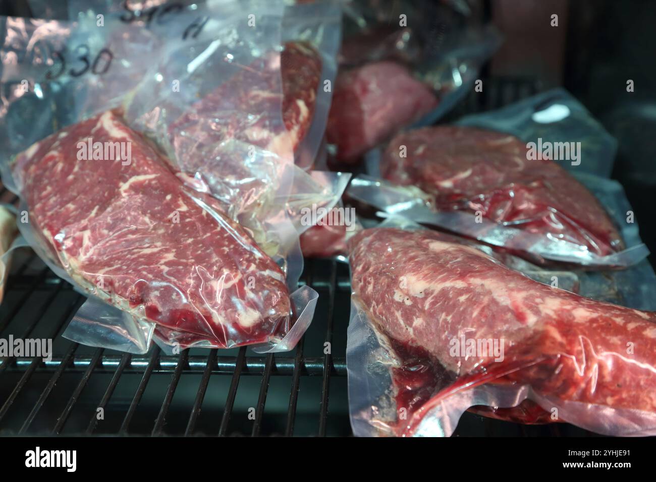 Rindersteaks werden in einem speziellen Kühlschrank aufbewahrt, bevor sie gekocht werden. Steaks in luftdichten Verpackungen im Kühlschrank. Reifung von Steaks vor dem Kochen. Stockfoto