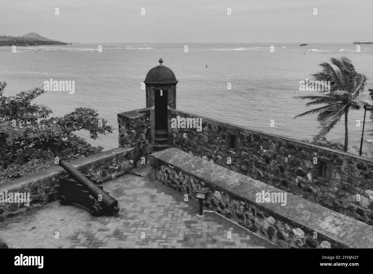 Eine Küstenbefestigung steht am Meer, mit einer Steinmauer und einer alten Kanone mit Blick auf den Ozean. Palmen schwanken sanft in der Brise, Addin Stockfoto