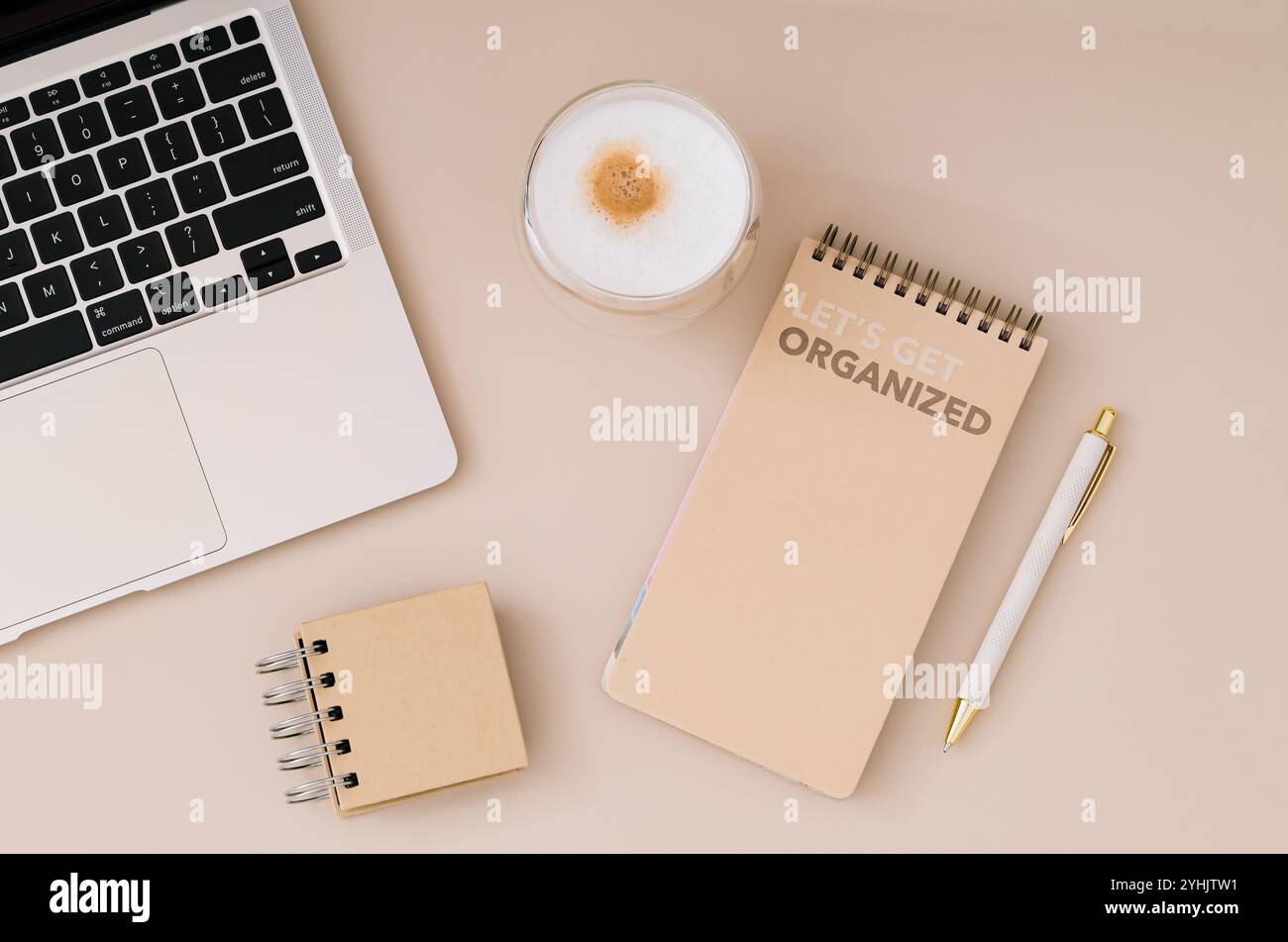 Trendiges Layout mit Planer, Computer, Kaffee und Stift auf beigefarbenem Hintergrund. Planer für Organisations- und Zielprioritäten. Stockfoto