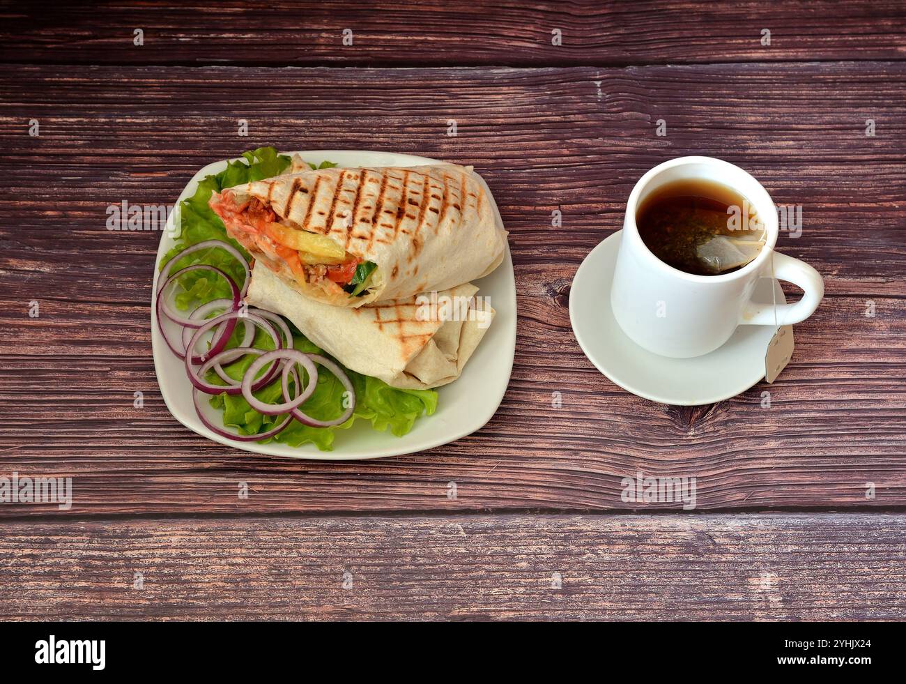 Frische, saftige Shawarma mit Fleisch auf einem Salatblatt mit Stücken roter Zwiebeln und einer Tasse schwarzen Tee auf einem dunklen Holztisch. Draufsicht, flach. Stockfoto