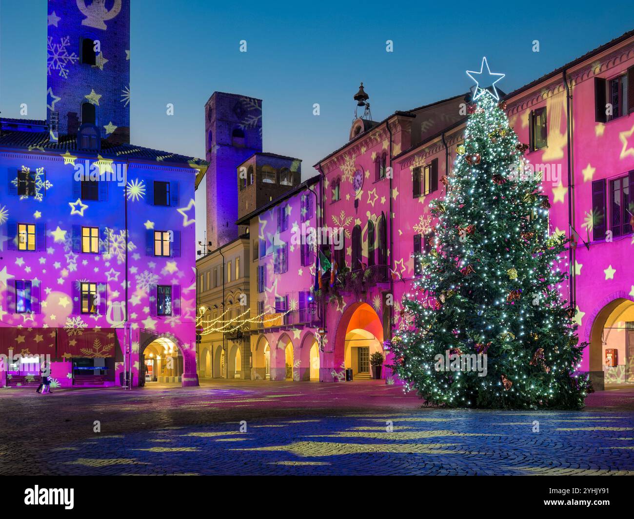 Abendblick auf einen festlichen Stadtplatz, der für die Weihnachtszeit dekoriert ist, und großen Weihnachtsbaum mit Lichtern in Alba, Italien. Stockfoto