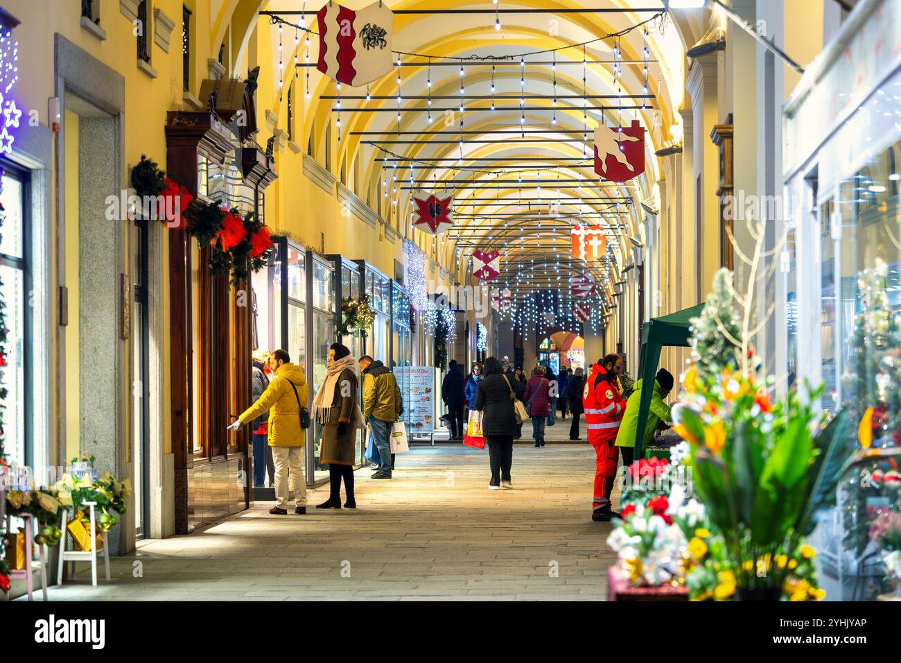 Menschen gehen entlang beleuchteter Geschäfte in der mit Weihnachtslicht geschmückten Galerie für die Winterferien in Asti, Italien. Stockfoto