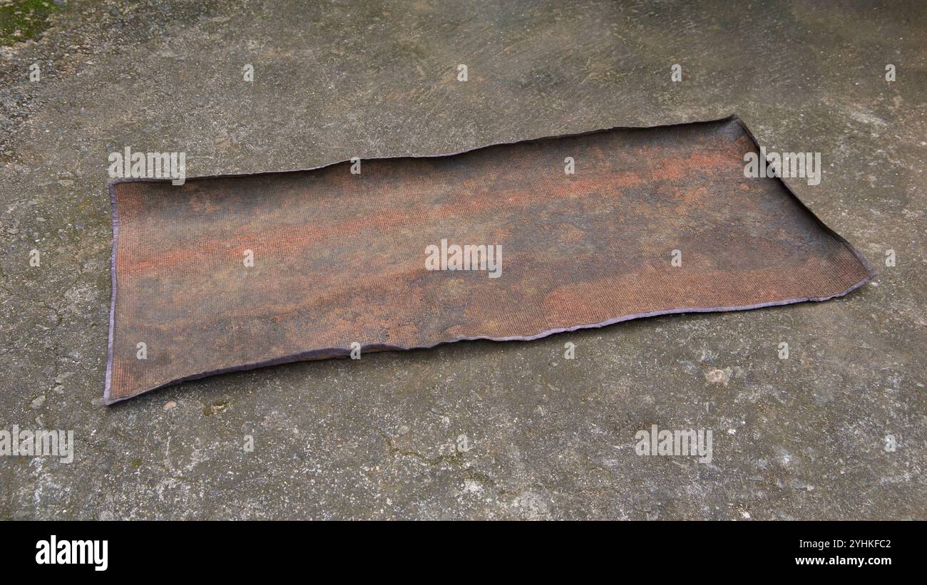 Benutzter alter, verwitterter, schmutziger Teppich auf Zementoberfläche, verblasster, ausgefranster Schmutz oder Staub gesammelt und steife Matte im weichen Fokus Stockfoto