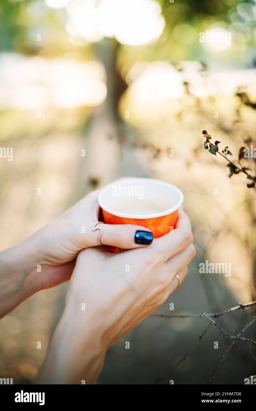 Schöne weibliche Hände mit schwarz bemalten Nägeln, die eine Tasse Kaffee mit verschwommenem Hintergrund halten. Stockfoto