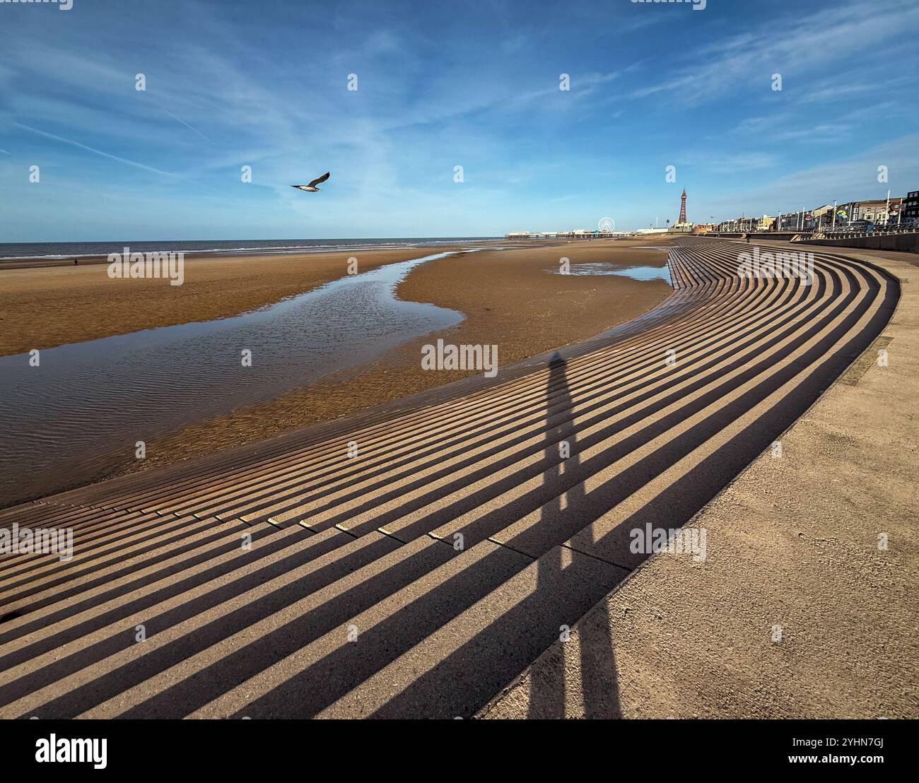 Schatten einer Figur auf Stufen der Meeresmauer an der Küste von Blackpool mit Blick auf North Pier und Blackpool Tower - Smartphone-aufgenommenes Stockfoto Schatten einer Figur auf Stufen der Meeresmauer an der Küste von Blackpool mit Blick auf North Pier und Blackpool Tower - Smartphone-aufgenommenes Stockfoto