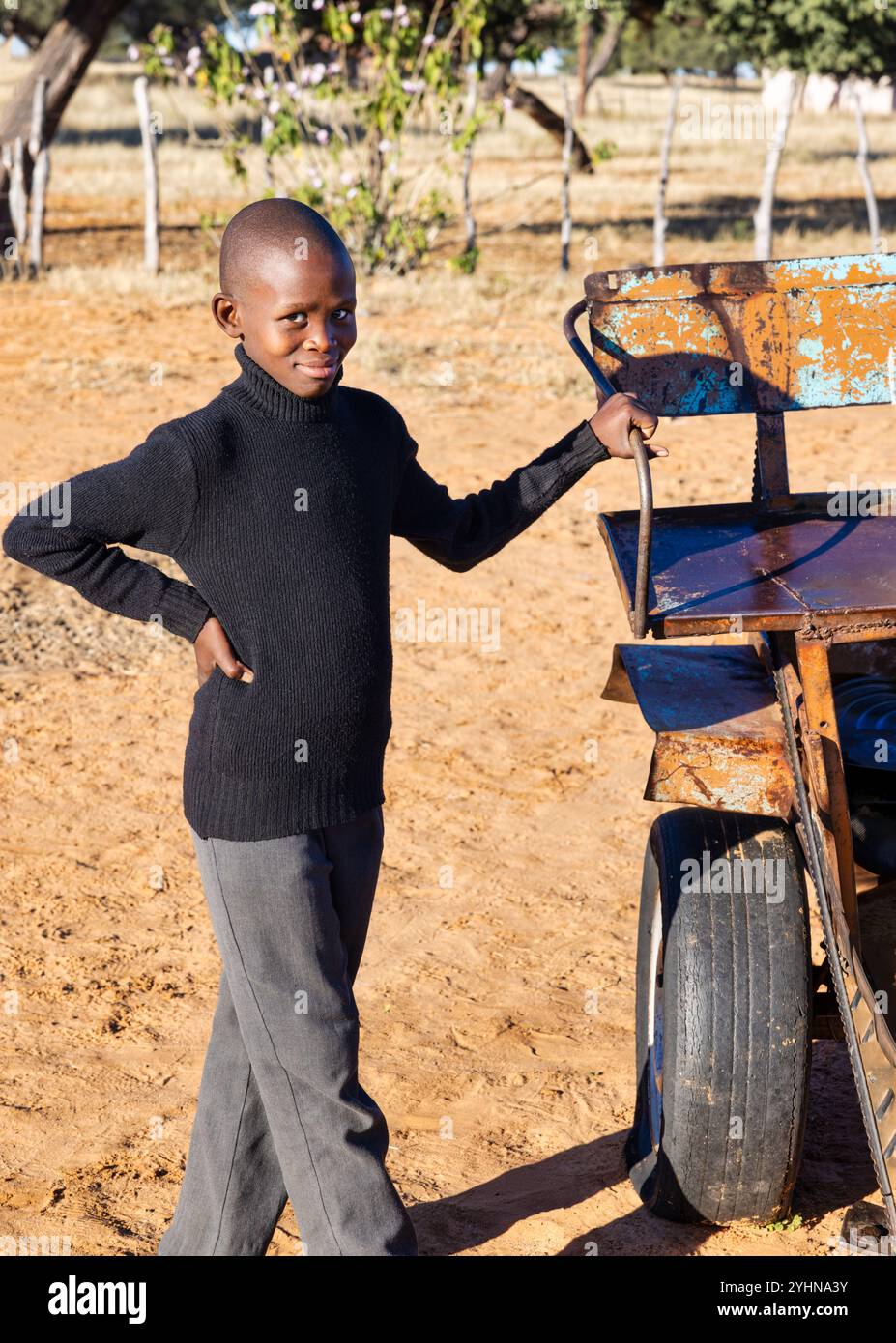 afrikanische Dorfbewohner, Junge, der sich an einem Wagen hält und ein schwarzes Rollkragentrikot trägt Stockfoto