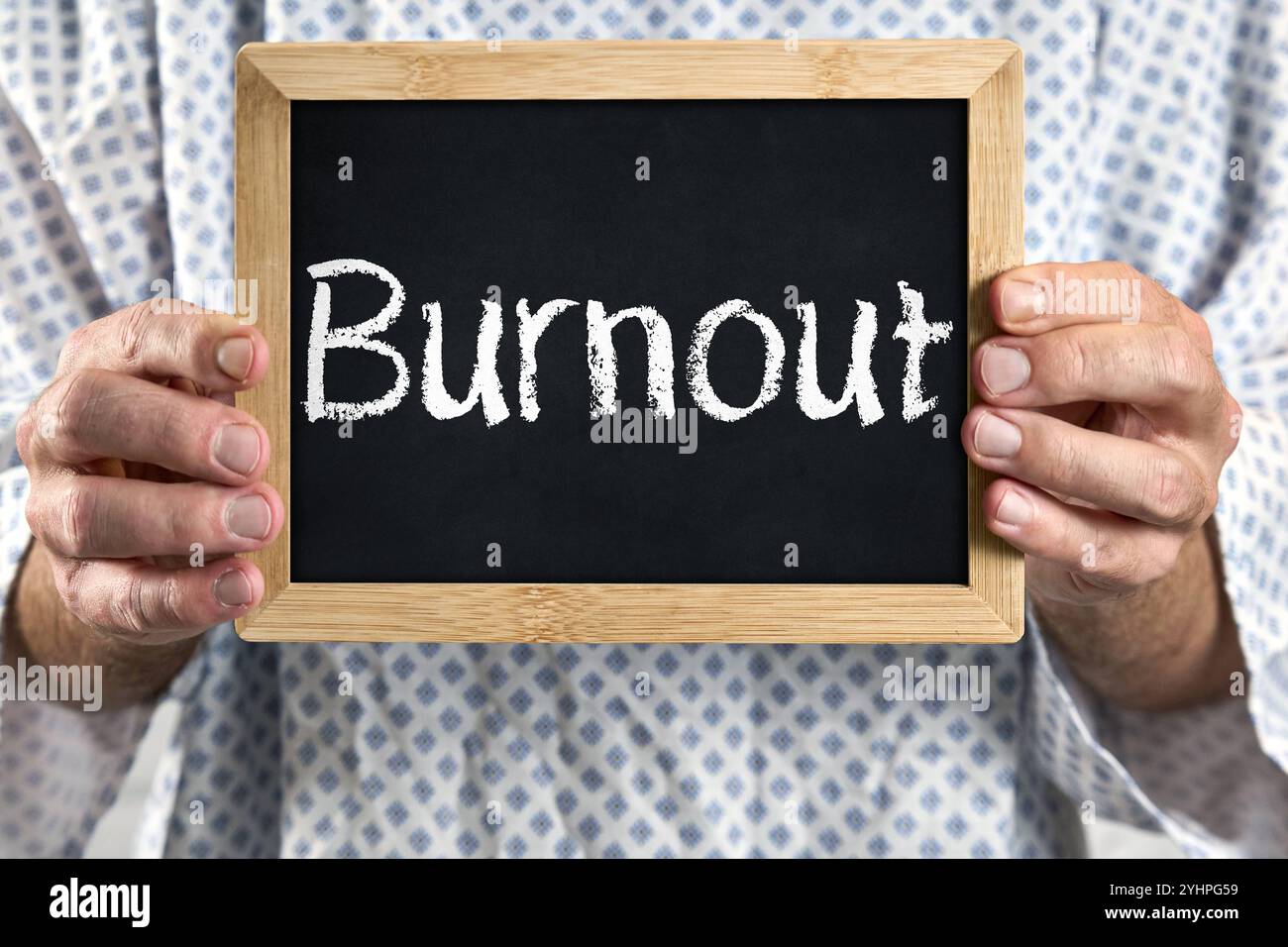 Bayern, Deutschland - 12. November 2024: Burnout, kranker Patient im Patientenkleid mit Schild. Symbolisches Bild für körperliche, emotionale und geistige Erschöpfung mit verminderter Leistung oder Krankheit - Überlastung und Krankheit, sowie Symptome. *** Burnout, Erkrankter Patient im Patientenkittel mit Schild. Symbolbild für körperliche, emotionale und geistige Erschöpfung mit reduzierter Leistungsfähigkeit bzw. Erkrankung - Überlastung und Krankheit, sowie Symptome. Stockfoto