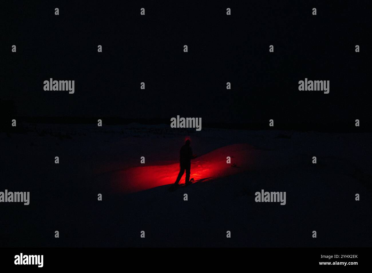 Eine Person im Schnee, die eine gruselige rote Taschenlampe in der dunklen Nacht leuchtet Stockfoto