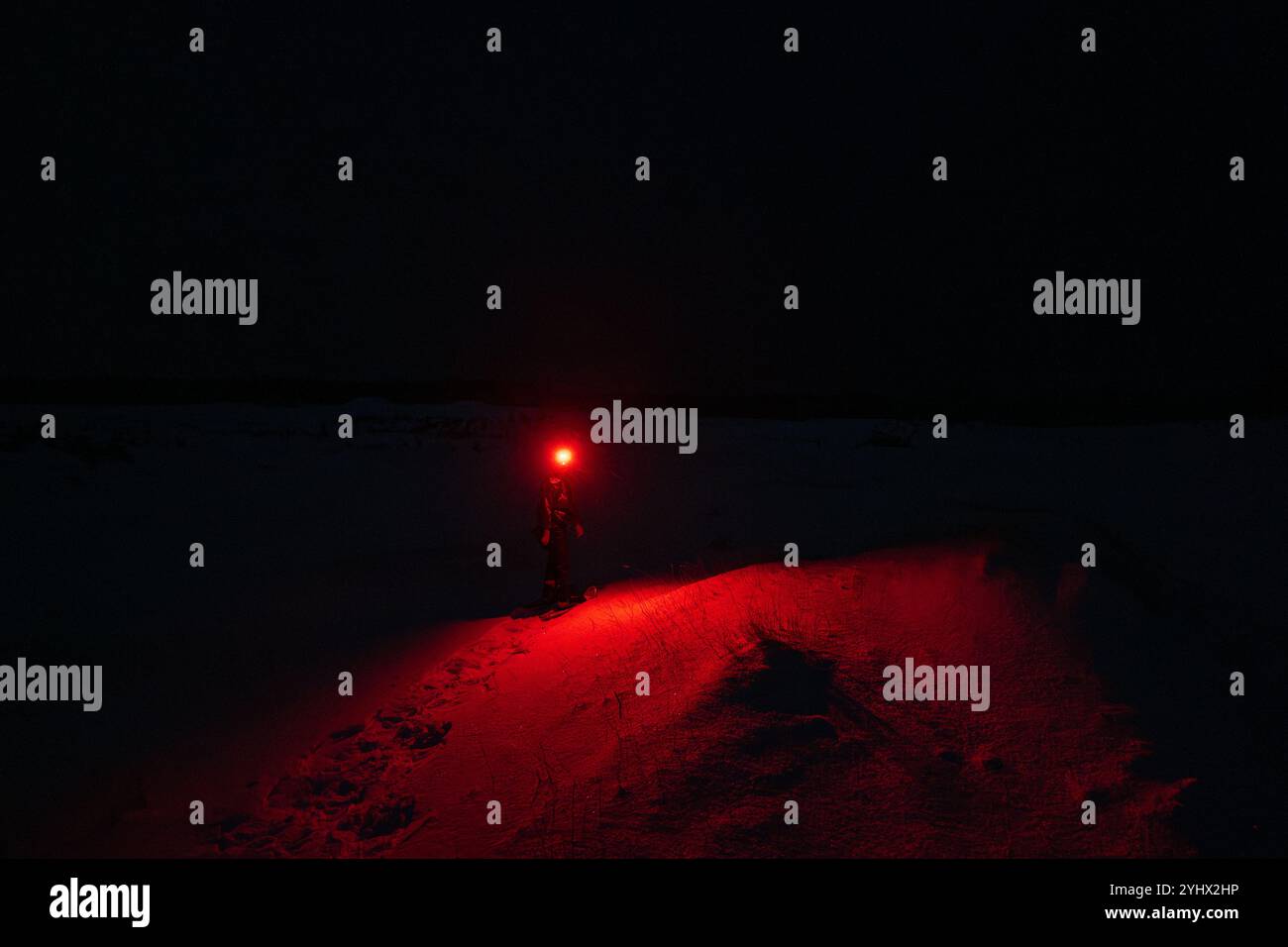 Eine Person im Schnee, die eine rote Taschenlampe im Dunkeln leuchtet Stockfoto