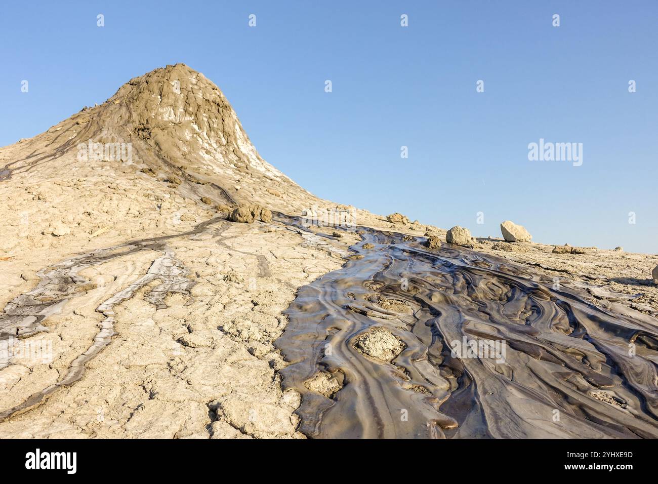 Natürliche Landschaft mit einem Schlammvulkan mit getrockneten und fließenden Schlammmustern unter einem klaren blauen Himmel bei Vulcanii Noroiosi, Rumänien Stockfoto