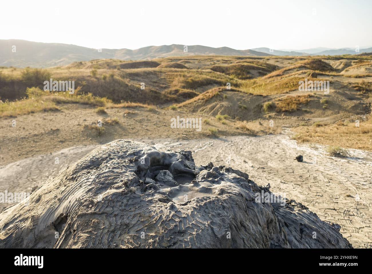 Trockener Schlammvulkan in einer kargen, zerrissenen Landschaft mit fernen Hügeln unter einem weichen Abendhimmel (Vulcanii Noroiosi, Rumänien) Stockfoto