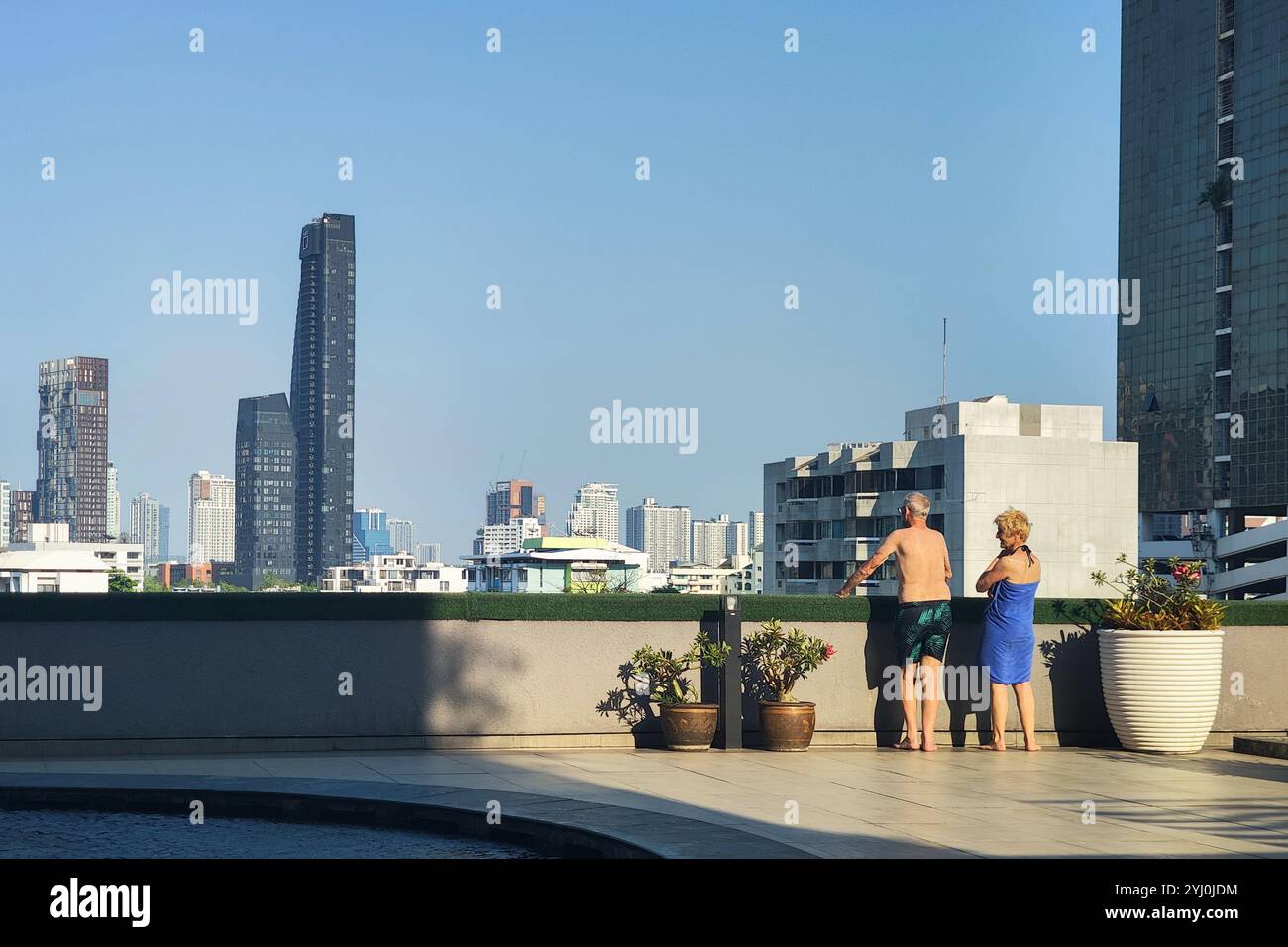 Bangkok, Thailand - 16. Oktober 2024 : ältere ältere ältere Ehepaare stehen am Pool auf dem Dach, mit Blick auf die moderne Skyline der Stadt im Hotel am Sommertag. Stockfoto