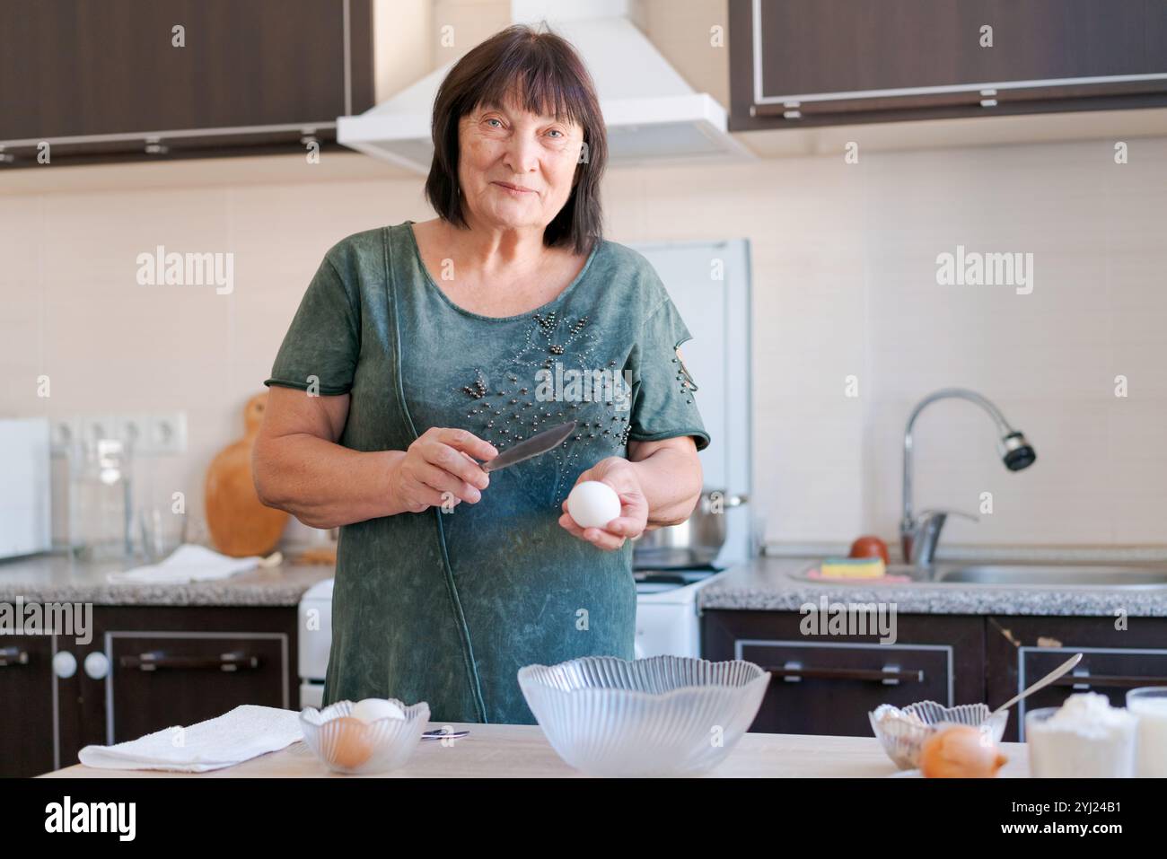 Die Frau schneidet ein Ei in einer Küche. Sie trägt ein grünes Hemd und hält ein Messer Stockfoto
