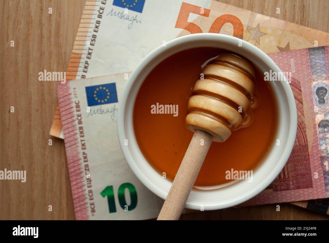 Eine Schüssel Bio-Honig mit einem hölzernen Honiglöffel, umgeben von Bienenpollenkörnern und Kamillenblüten auf dunkelblauem Hintergrund. Stockfoto