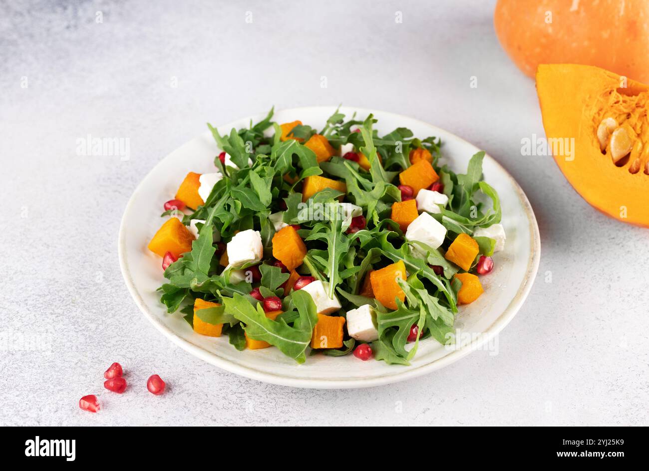Kürbissalat mit Rucola, Fetakäse und Granatapfelkernen auf grauem Hintergrund. Draufsicht. Thanksgiving-Gerichte. Stockfoto