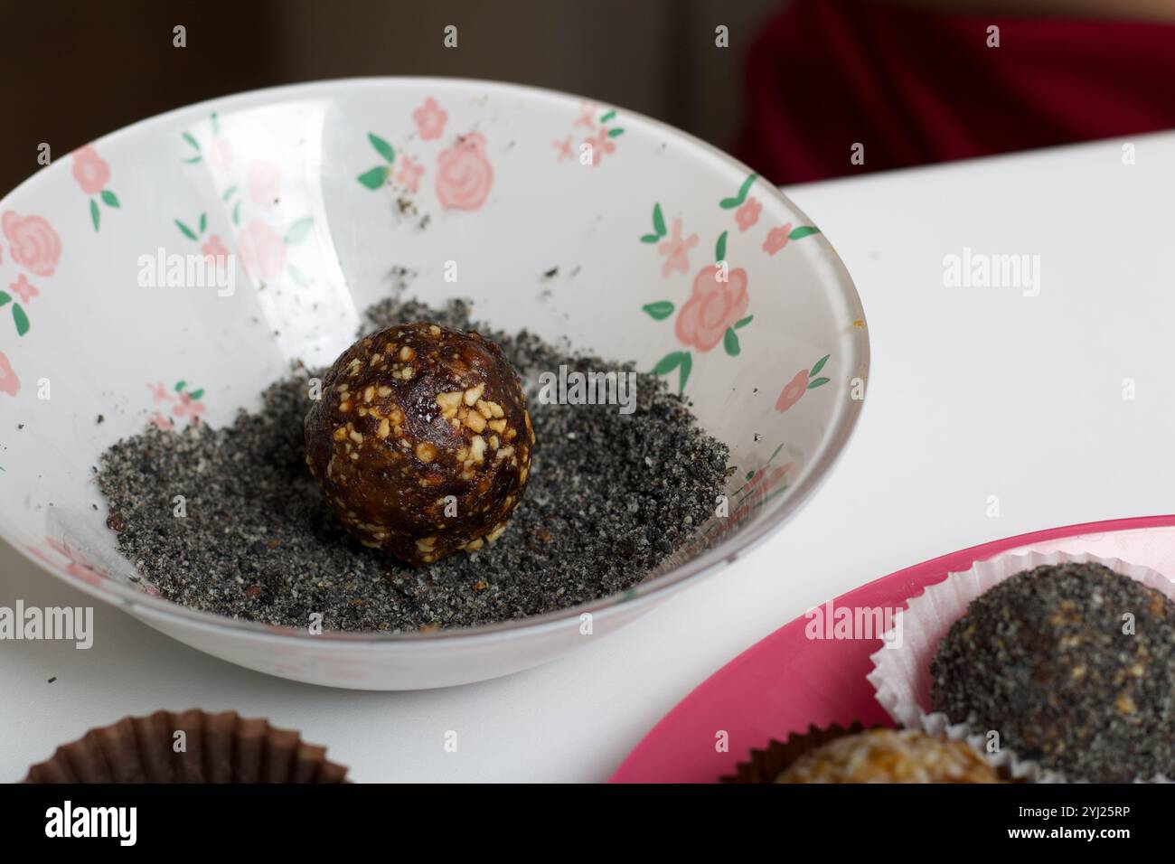 Getrocknete Fruchtbonbons. Von Pflaumen, Datteln und Kokosnuss. Liegt auf einem Spritzer schwarzem Sesampulver. Stockfoto