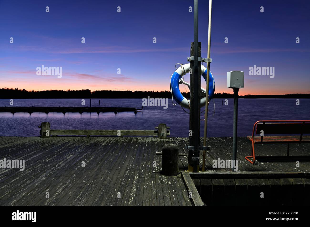 Eine ruhige Hafenlandschaft am See bei Sonnenuntergang oder Dämmerung, mit einem leuchtenden Himmelsverlauf, der von Orange und Rosa am Horizont zu tiefblauem Himmel übergeht Stockfoto