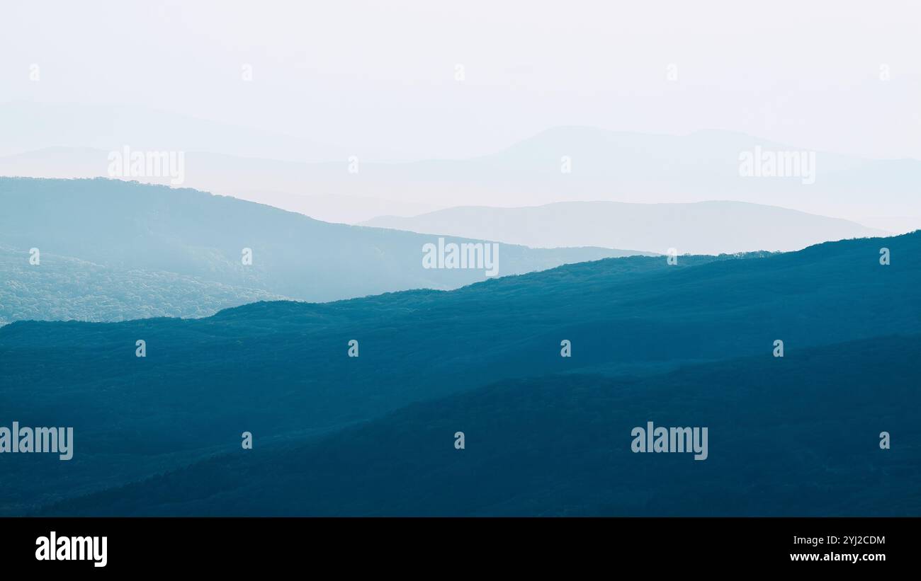 Bergkette mit sichtbaren Silhouetten durch den farbenfrohen Nebel am Morgen. Ruhige abendliche Landschaft in den Bergen bei Sonnenuntergang. Fototapete. Natürliche bac Stockfoto