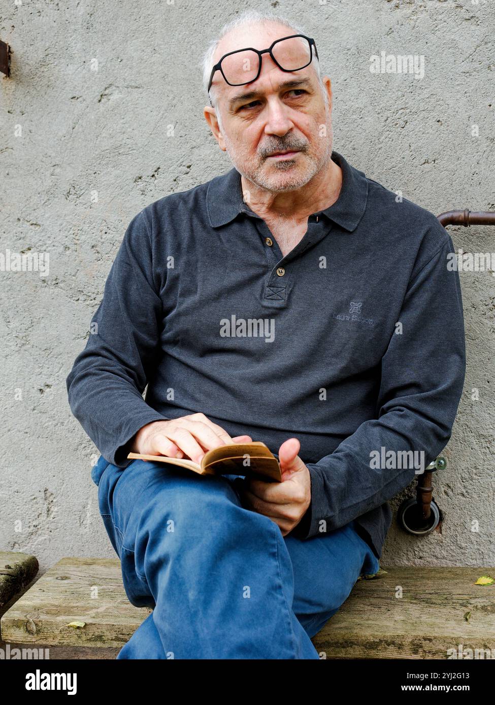 Reifer Mann mit einer Brille auf dem Kopf, sitzt und liest draußen ein kleines Buch, Italien Stockfoto