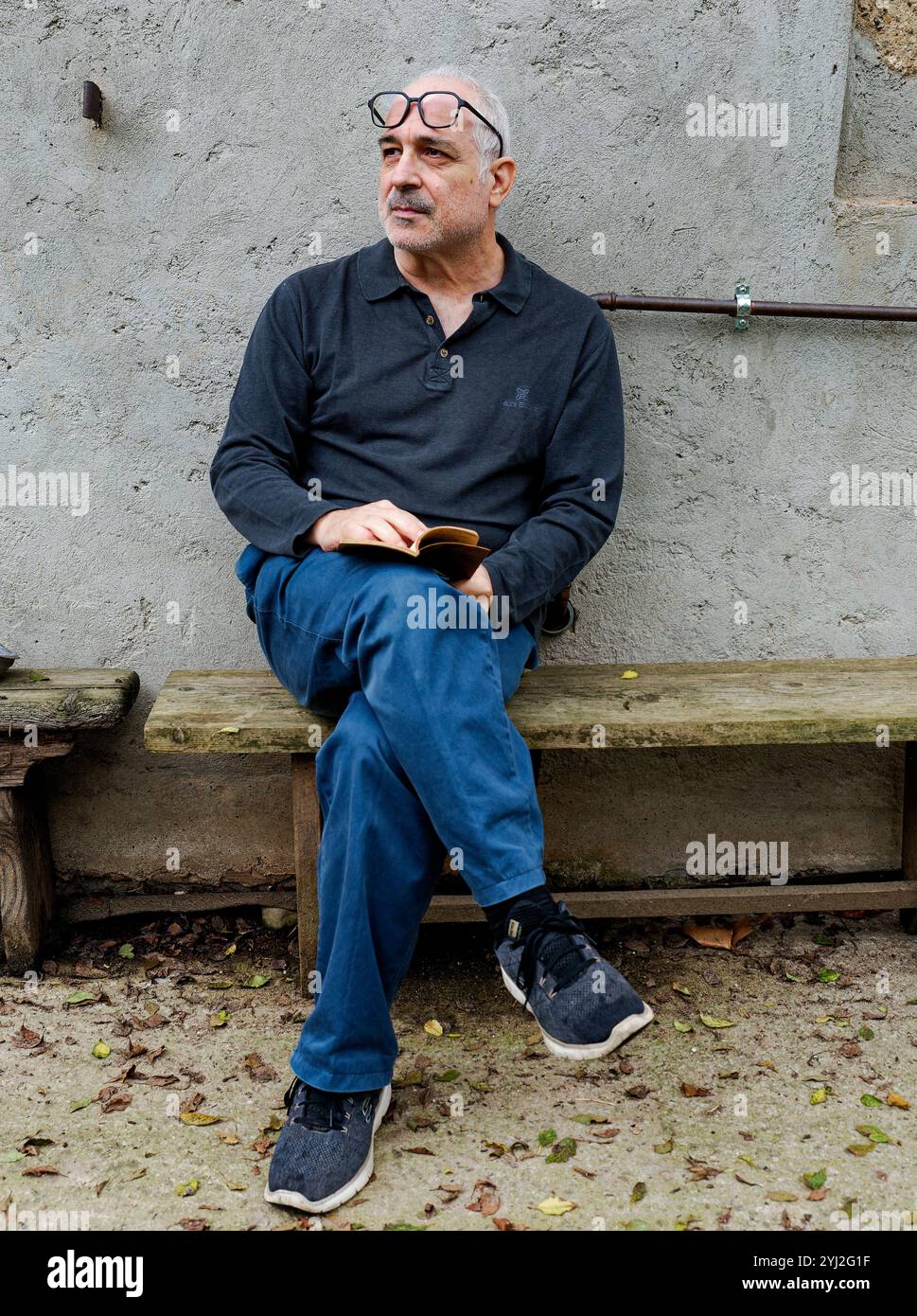 Mann, der draußen auf einer Bank sitzt und ein Buch hält und nachdenklich zur Seite blickt, Italien Stockfoto