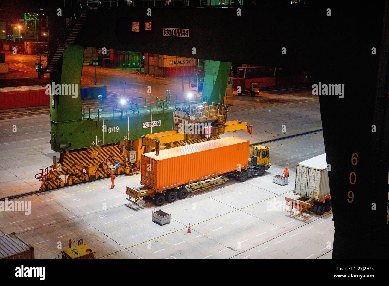 Eine nächtliche Szene an einem Schiffsterminal mit einem Portalkran, der einen Hapag-Lloyd-Container auf ein Frachttransportfahrzeug in Singapur transportiert Stockfoto