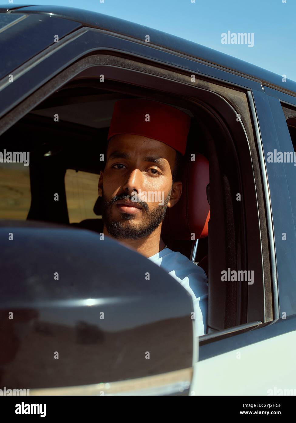 Mann mit rotem fez-Hut, der unter klarem Himmel durch das Autofenster schaut, Marokko Stockfoto