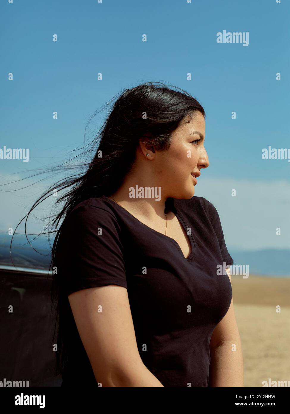 Frau in lässigem Outfit, die vor einem klaren Himmel steht und ihr Haar im Wind weht, Marokko Stockfoto