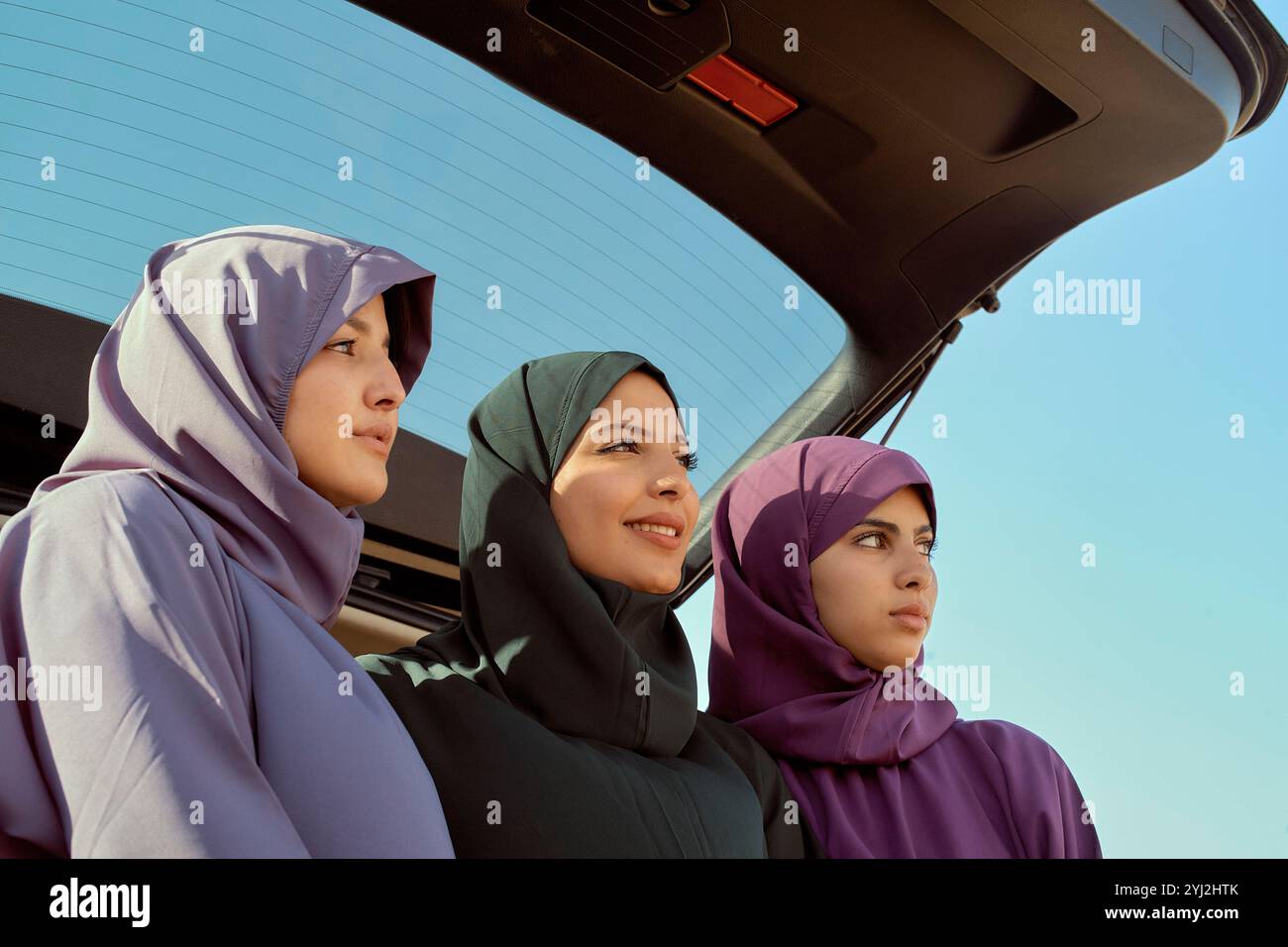 Drei Frauen in farbenfrohen Hijabs, die an einem sonnigen Tag in Marokko in die Ferne von der Rückseite eines Autos blicken Stockfoto Drei Frauen in farbenfrohen Hijabs, die an einem sonnigen Tag in Marokko in die Ferne von der Rückseite eines Autos blicken Stockfoto