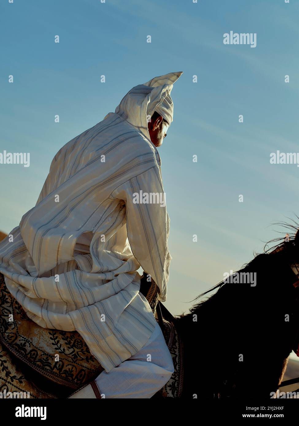 Eine Person in traditionellen weißen Gewändern zu Pferd vor klarem Himmel, Marokko Stockfoto