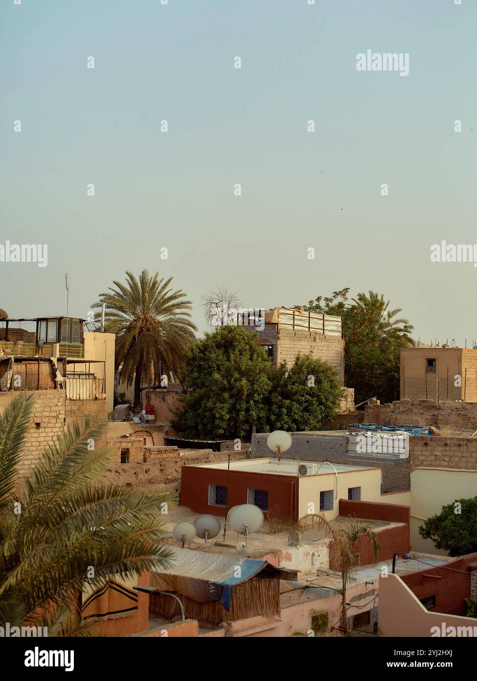 Sonnenuntergänge beleuchten die traditionelle Architektur und Palmen in einer nahöstlichen Stadtlandschaft, Marokko Stockfoto