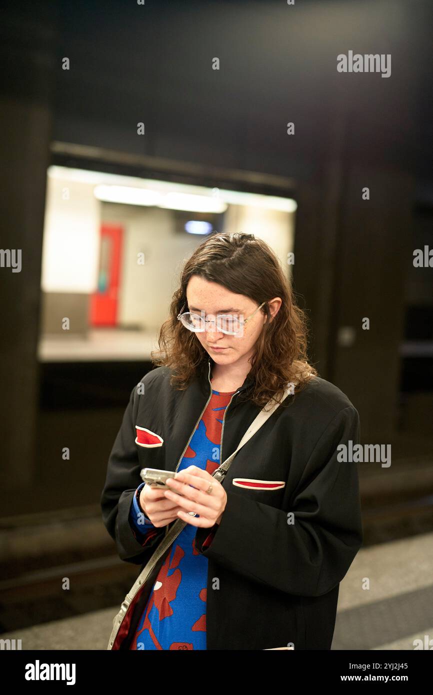 Frau mit Brille konzentrierte sich auf ihr Smartphone, während sie an einem Bahnsteig in Belgien stand Stockfoto