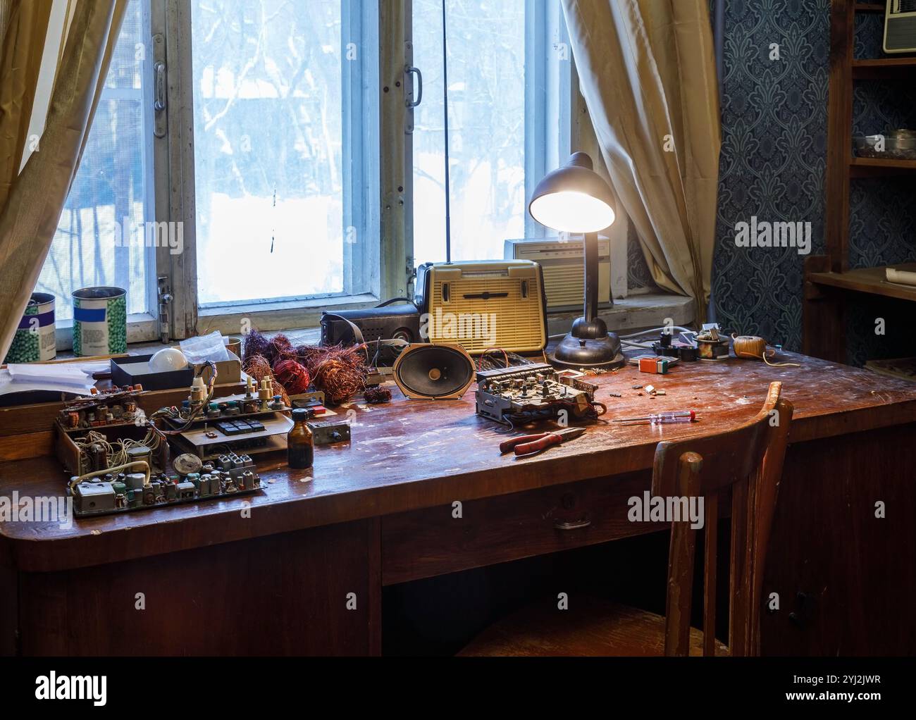 Das Innere einer alten Wohnung mit einem Holztisch, der mit Radioteilen übersät ist Stockfoto