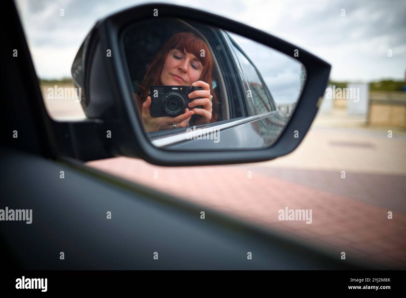 Die Frau macht ein Foto von sich in einem Autospiegel mit einer Kamera. Stockfoto