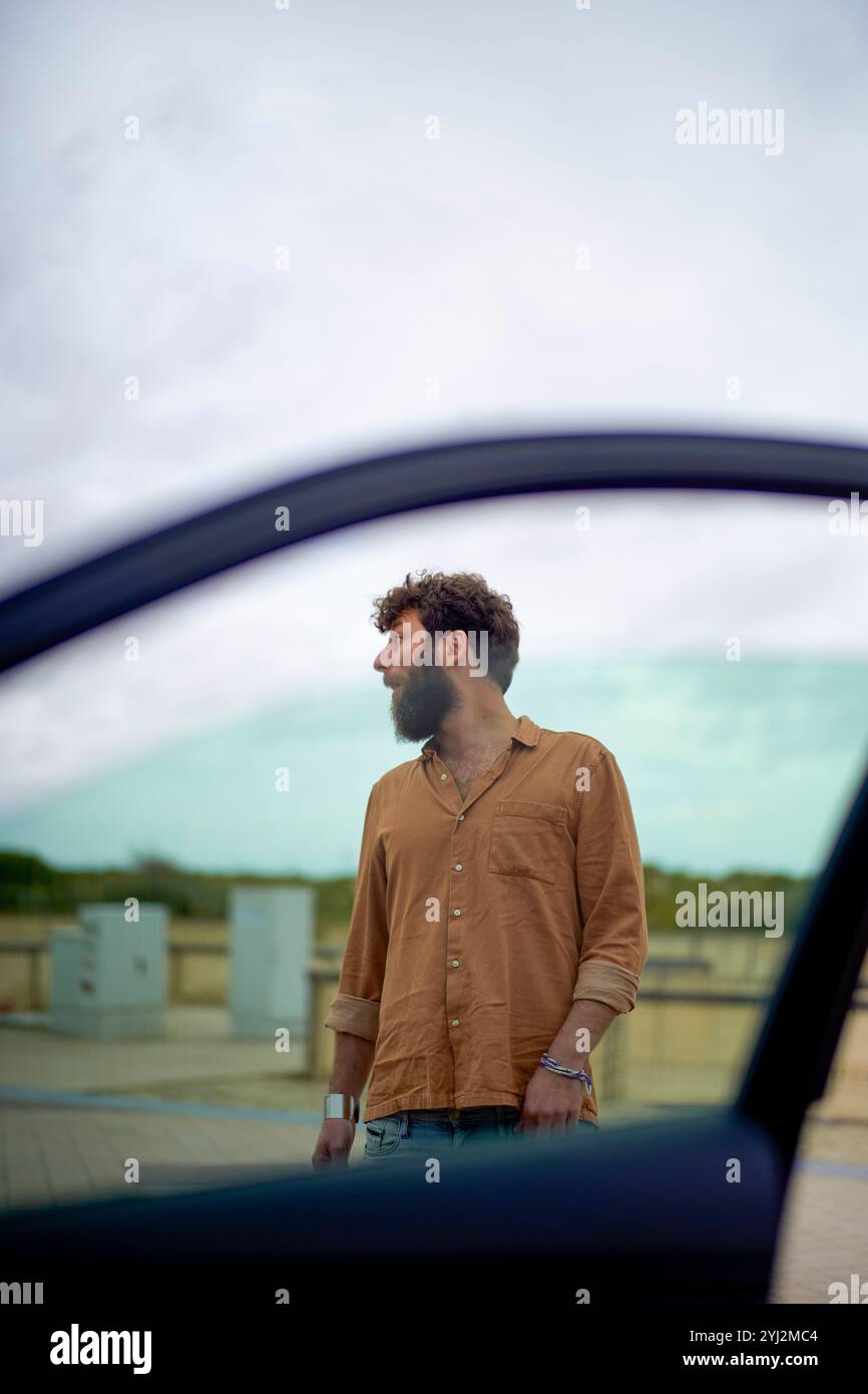 Mann, der durch ein Autofenster gesehen wird und in die Ferne blickt, vor einem bedeckten Himmel. Stockfoto