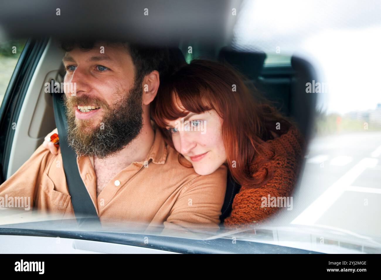 Lächelnder Mann, der ein Auto fährt, mit einer Frau, die sich auf der Schulter beugt und beide auf einer Roadtrip nach vorne blickt. Stockfoto