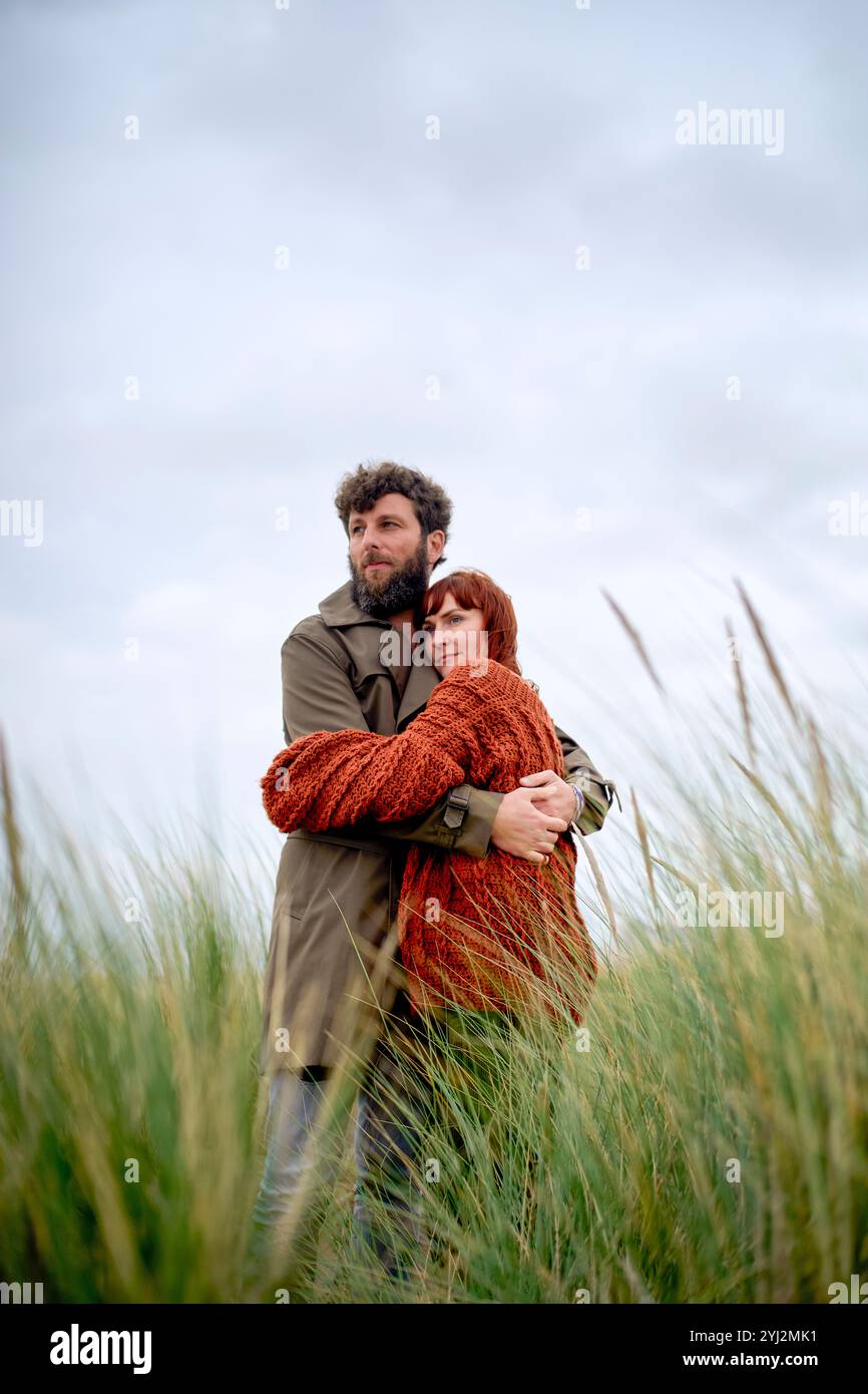 Ein Mann und eine Frau umarmen sich in einem Feld von hohem Gras vor einem bewölkten Himmel, Belgien Stockfoto