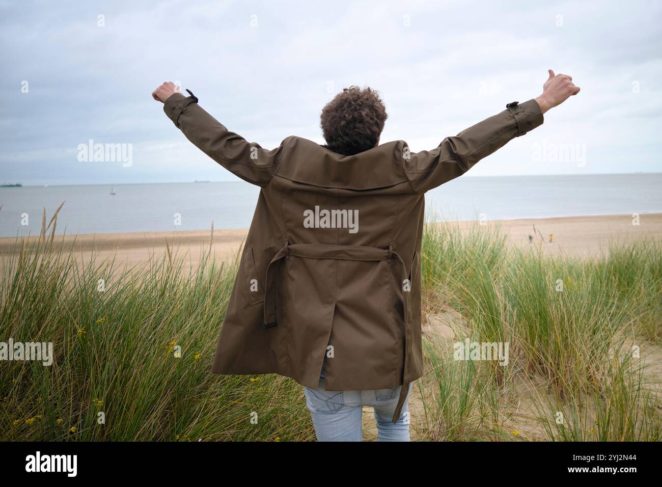 Person mit erhobenen Armen, die an einem Strand mit bewölktem Himmel steht, Belgien Stockfoto