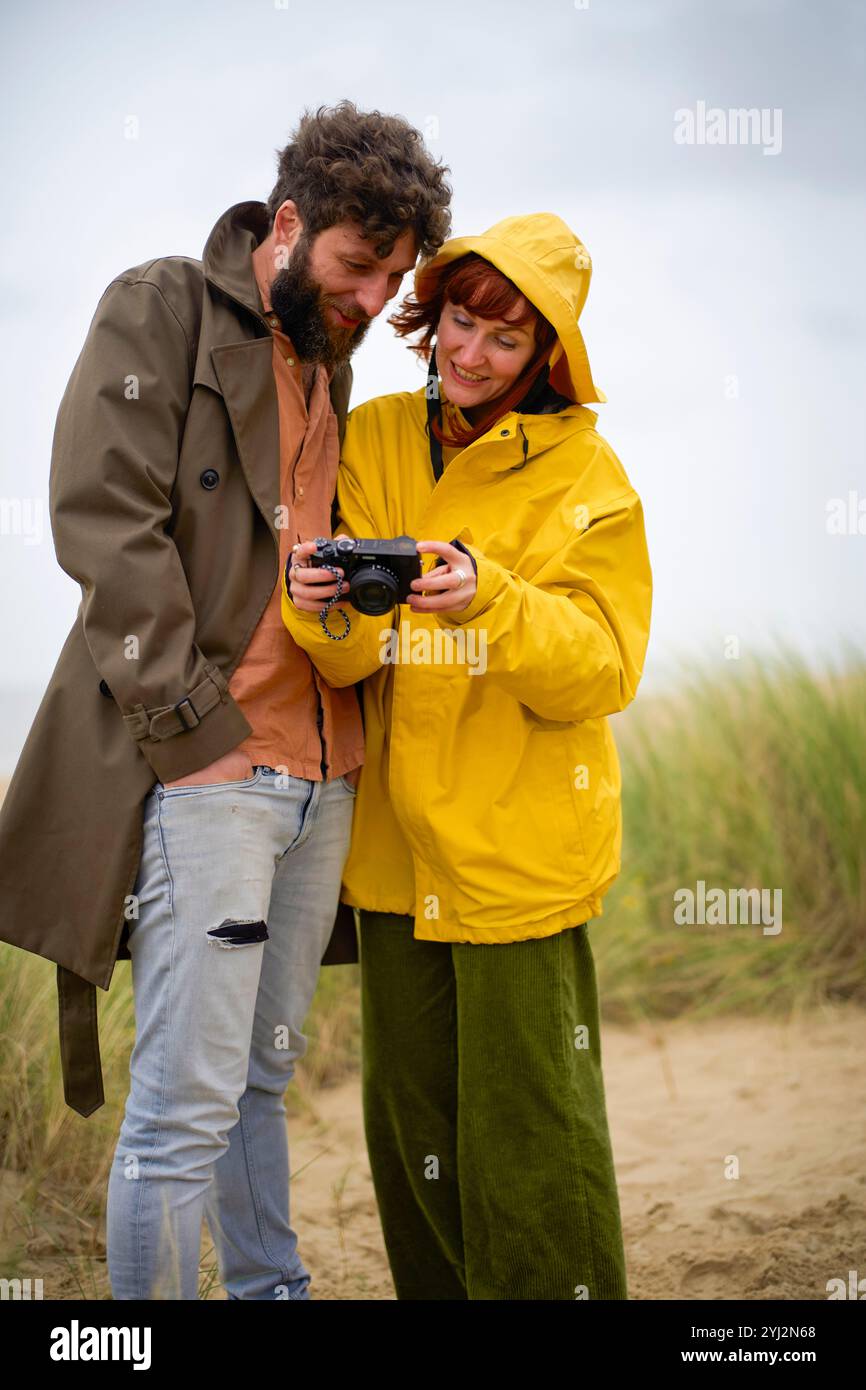 Ein paar Bewertungen Fotos auf einer Kamera, bequem in Jacken gekleidet an einem Strand mit hohem Gras, Belgien Stockfoto