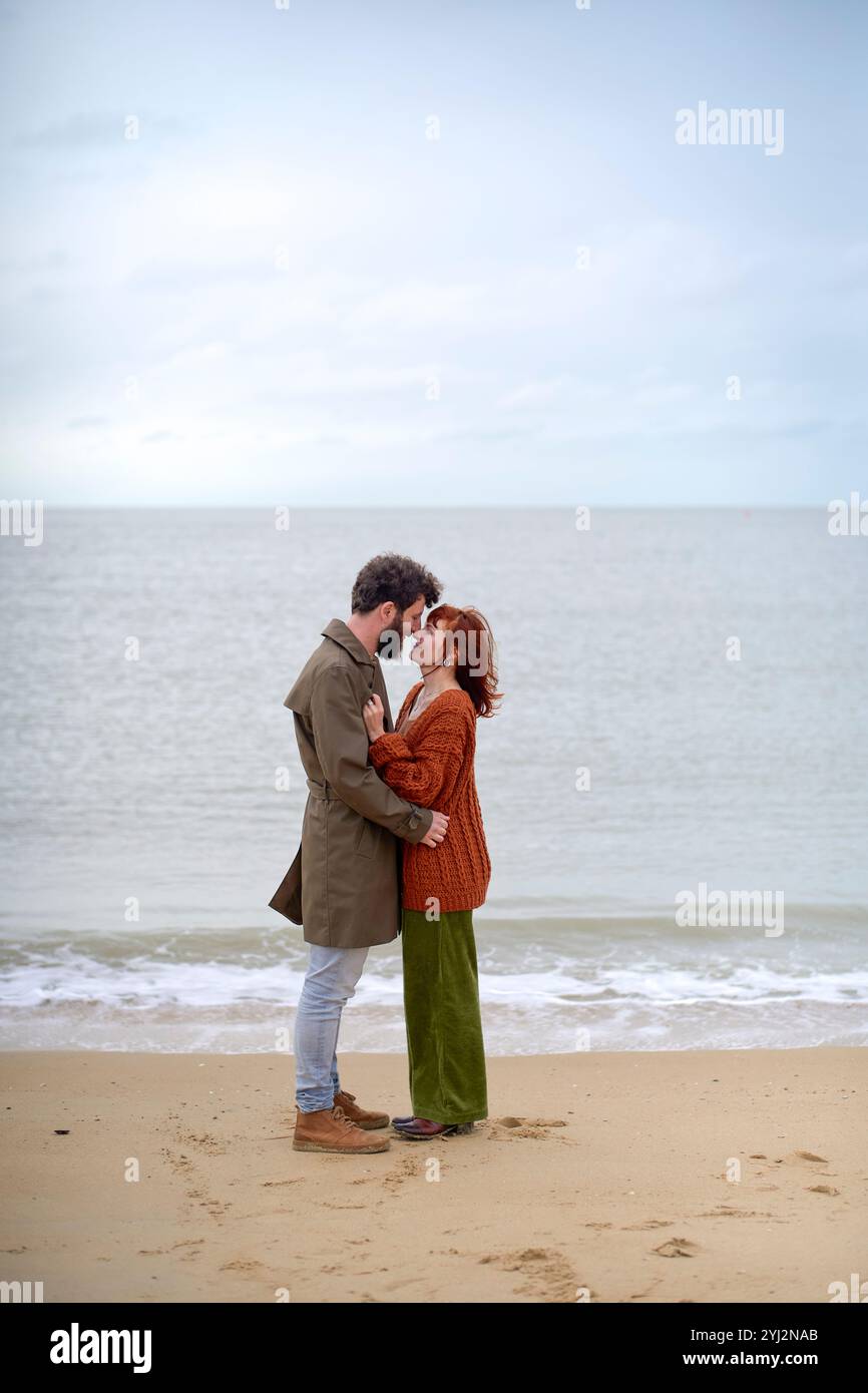 Ein Paar umarmt und teilt einen Kuss an einem Sandstrand mit bewölktem Himmel über Belgien Stockfoto