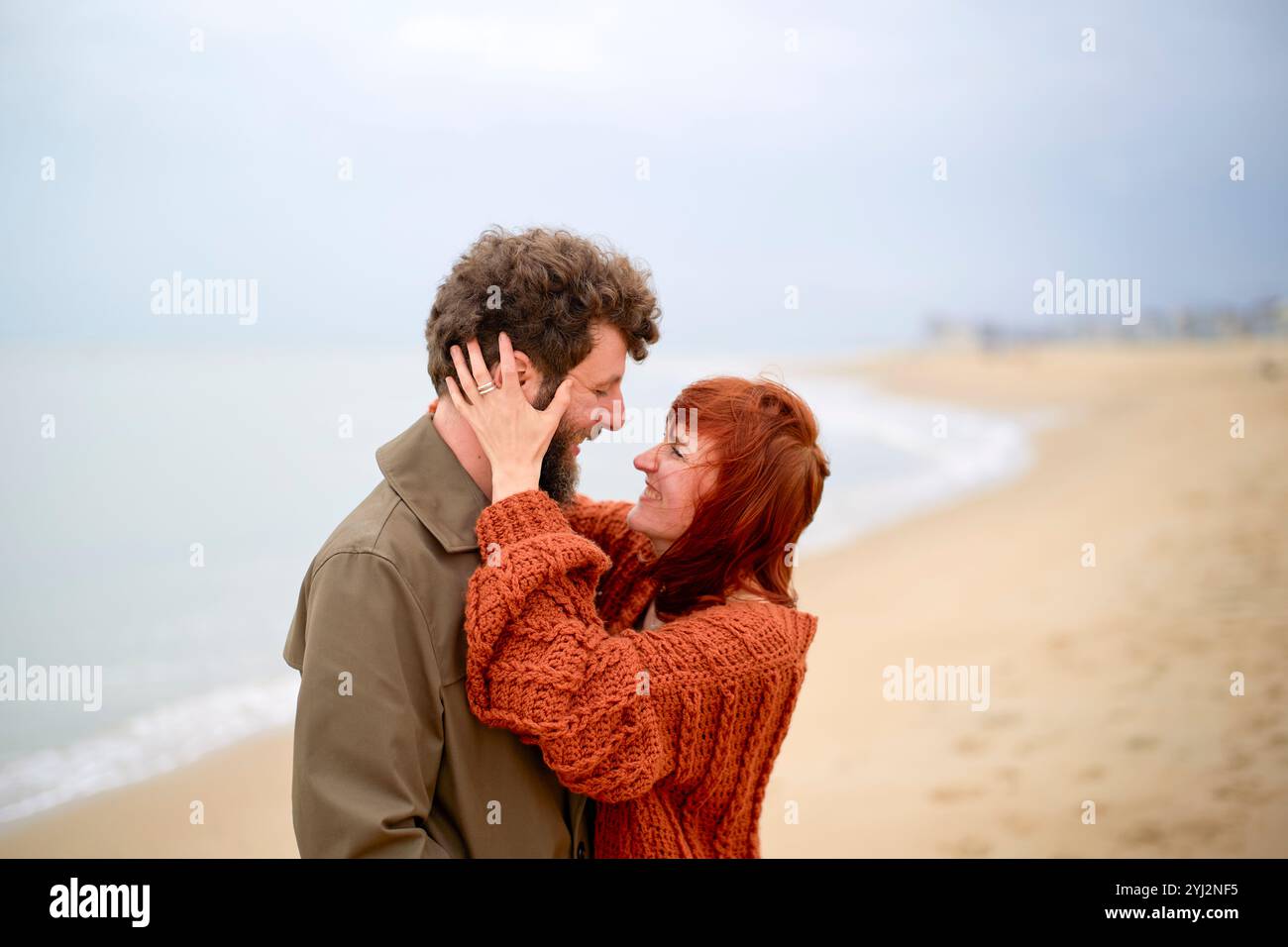 Ein liebevolles Paar umarmt und schaut sich gegenseitig in die Augen an einem einsamen Strand mit bewölktem Himmel, Belgien Stockfoto