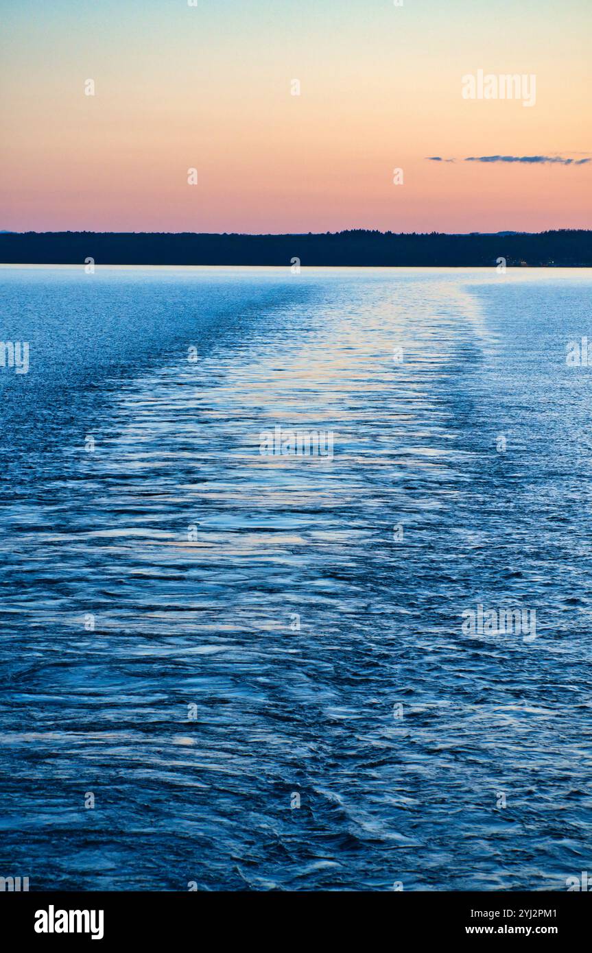 Blick von einem Schiff, das bei Sonnenuntergang von einer Insel auf dem Meer abfährt. Skandinavische Natur Stockfoto