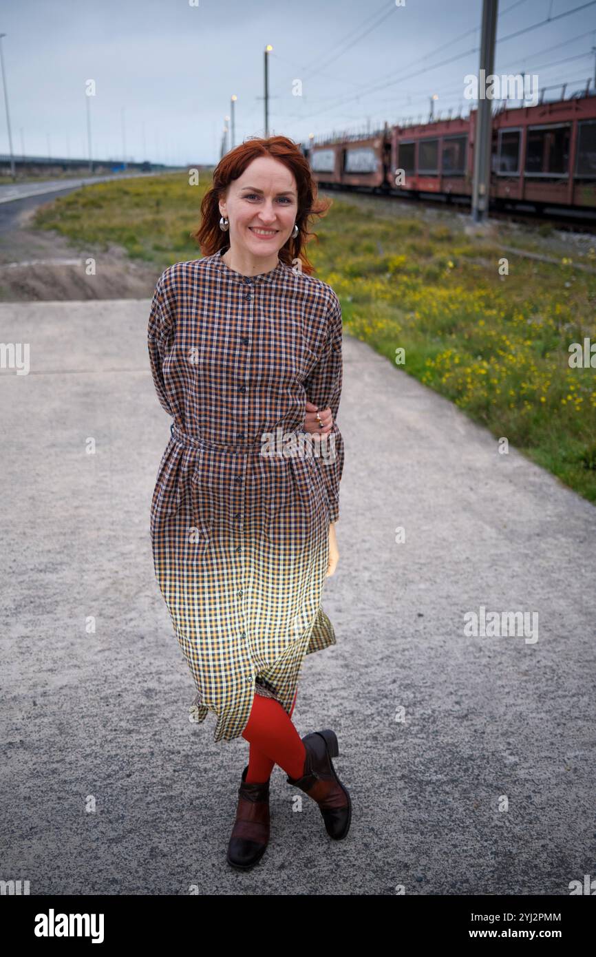 Lächelnde Frau mit rotem Haar, die während der Abenddämmerung auf einem Weg steht, mit einem Zug im Hintergrund. Stockfoto Lächelnde Frau mit rotem Haar, die während der Abenddämmerung auf einem Weg steht, mit einem Zug im Hintergrund. Stockfoto