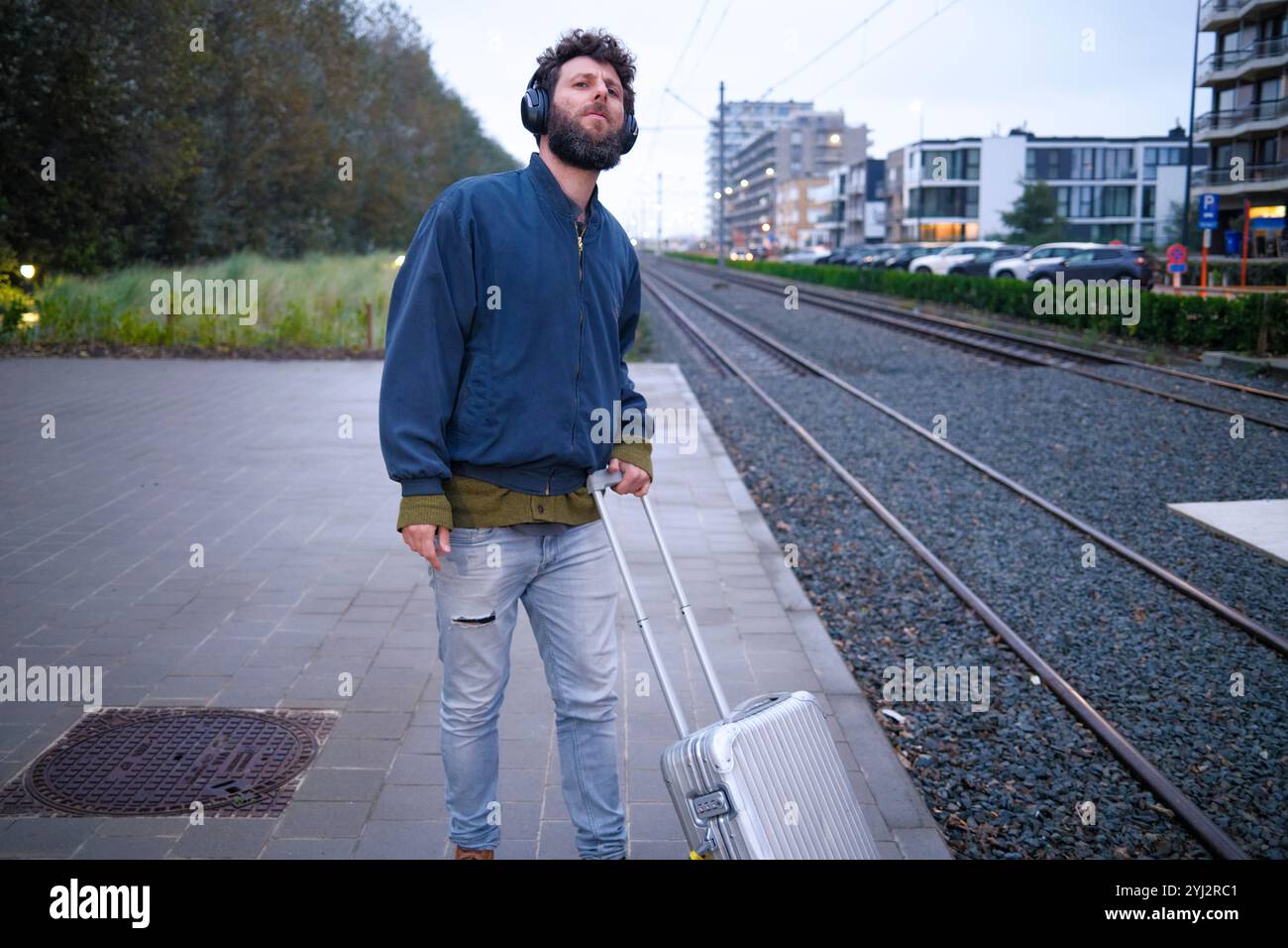 Mann, der mit einem Koffer an den Bahngleisen steht und mit aufmerksamem Ausdruck aufblickt, Belgien Stockfoto