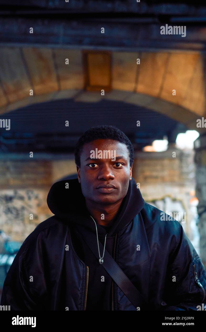 Selbstbewusster junger Mann in einer schwarzen Jacke unter einer Brücke, Berlin, Deutschland Stockfoto