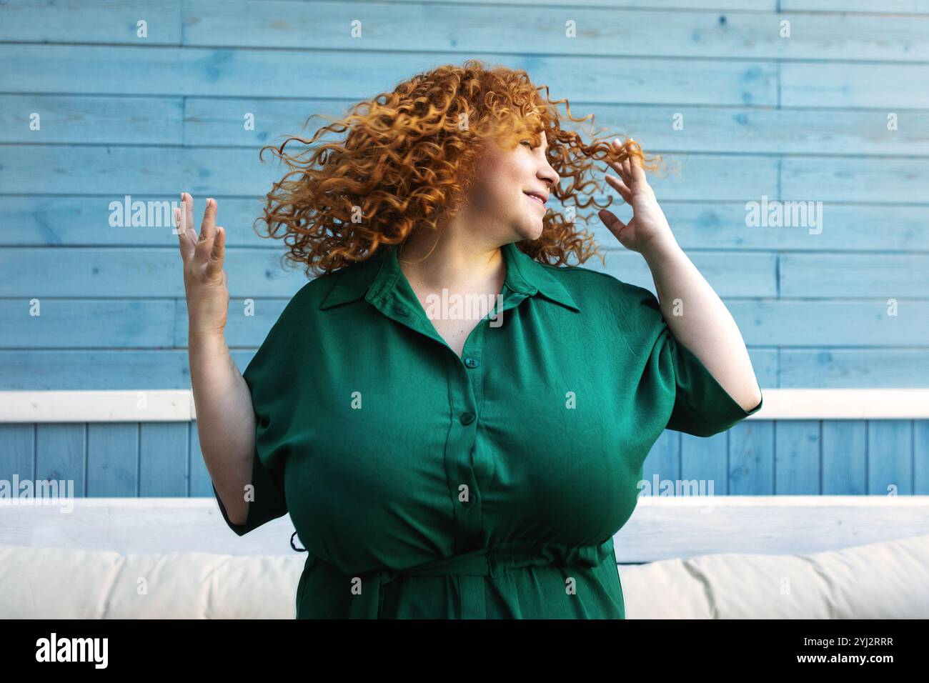 Schöne Happy Plus Size Frau genießt das Leben, tanzt und schüttelt Haare mit Freude, Selbstvertrauen und positiven Emotionen draußen vor blauem Hintergrund Stockfoto