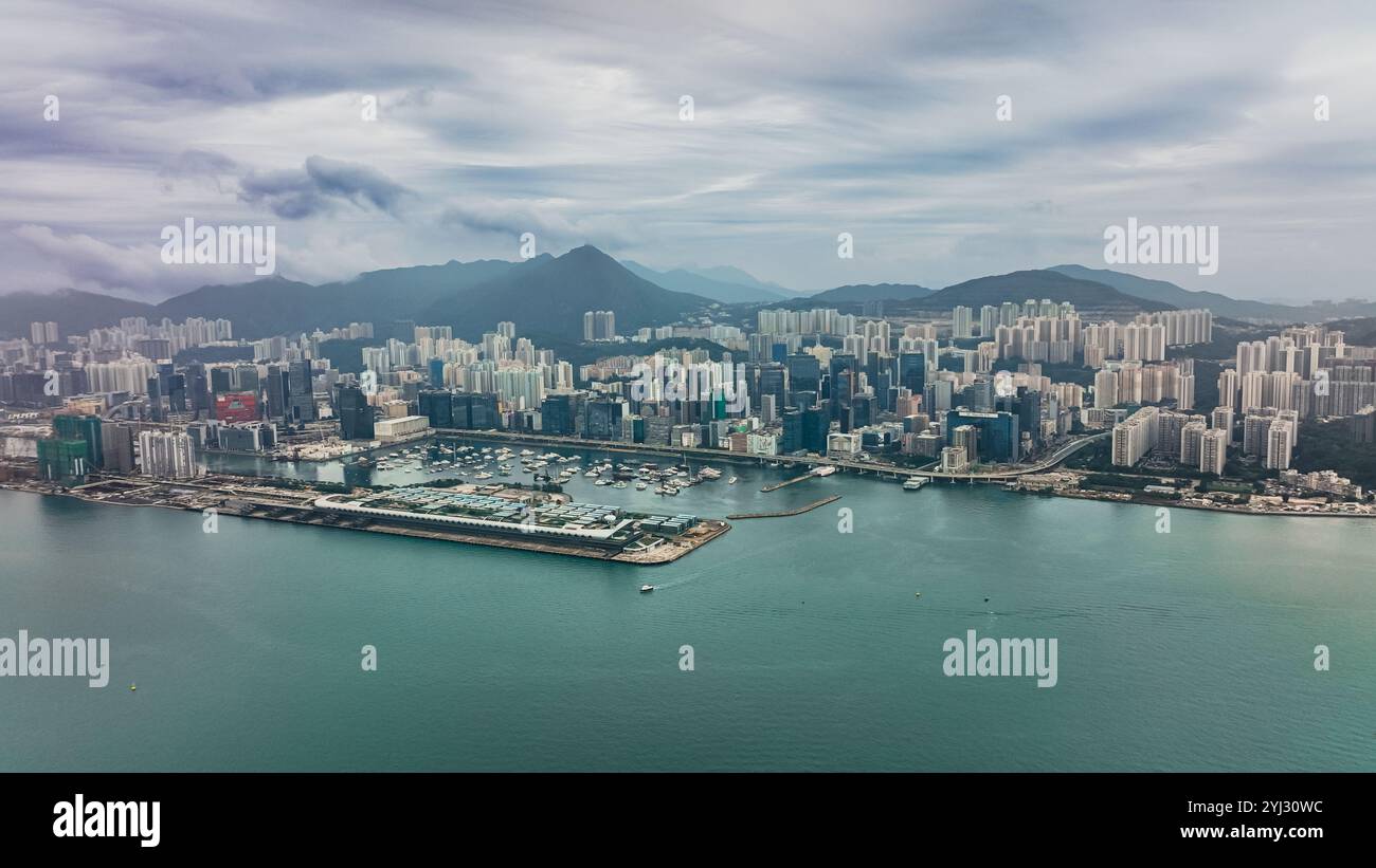 Der Blick fängt Victoria Bay mit einer geschäftigen Skyline, hoch aufragenden Gebäuden und Bergen im Hintergrund ein, die die urbane Landschaft von Hongkong widerspiegeln. Stockfoto