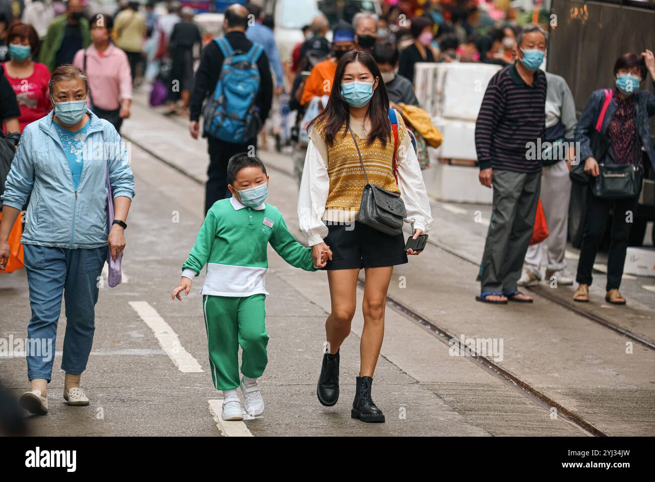 Familien und Einzelpersonen schlendern durch eine lebhafte Straße im Zentrum von Hongkong, alle tragen Masken, während sie durch die Menschenmassen navigieren. Stockfoto