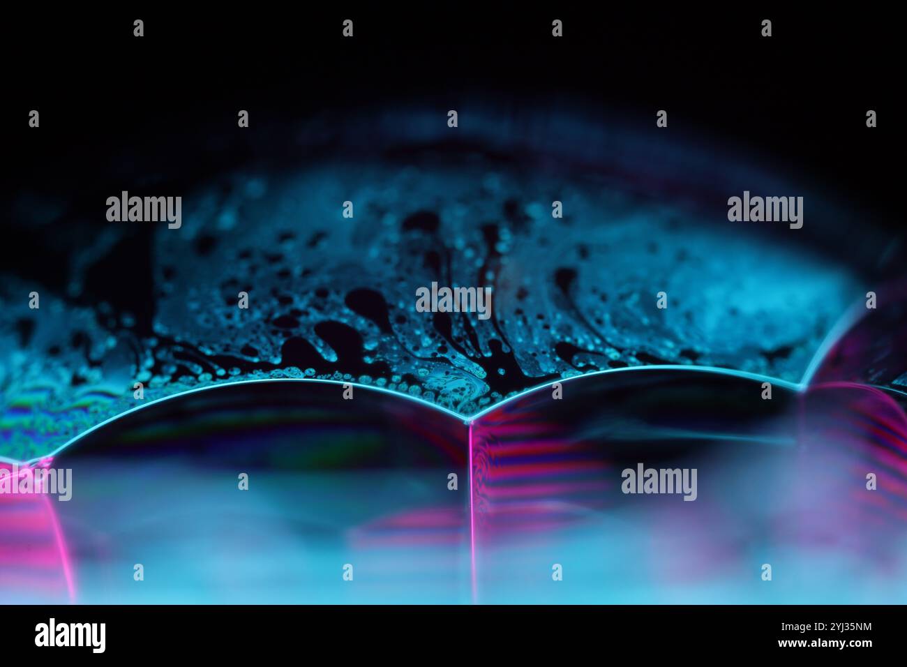 Hellblaue Flüssigkeit auf schwarzem Hintergrund, Ölflecken Bewegung, helle Chemie, surrealer Hintergrund, blaue Himmelsfarbe Stockfoto