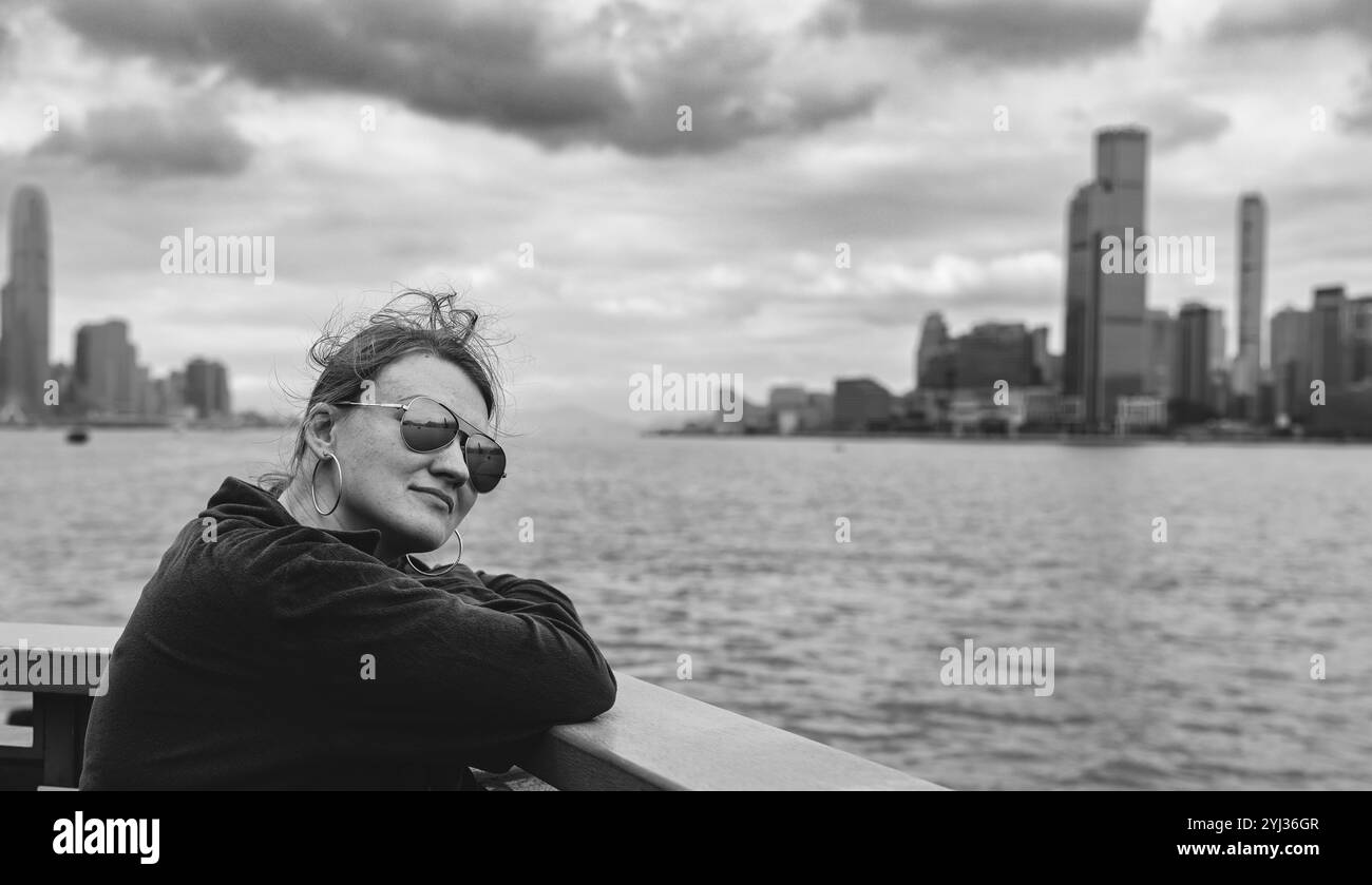 Ein Tourist lehnt sich an das Geländer und bewundert die Aussicht auf Hongkong und seine Skyline unter einem bewölkten Himmel. Stockfoto