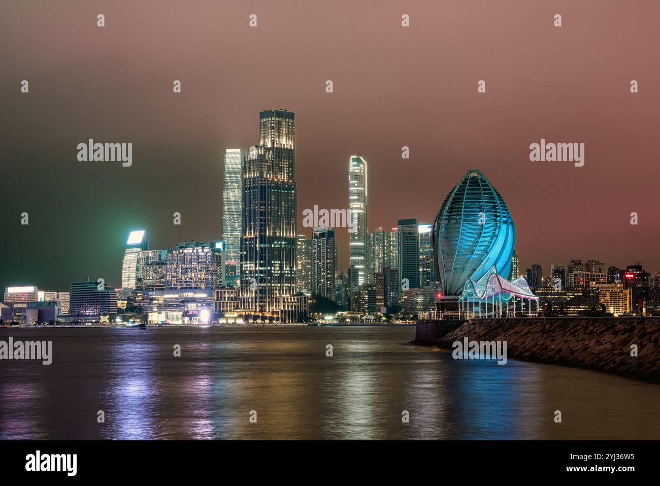 Helle Wolkenkratzer reflektieren den Hafen und zeigen Hongkongs pulsierende Stadtlandschaft vor einem Nachthimmel voller Wolken. Stockfoto